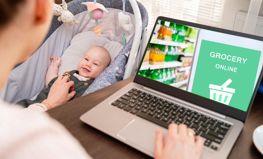 Mother buying groceries online, while soothing infant.