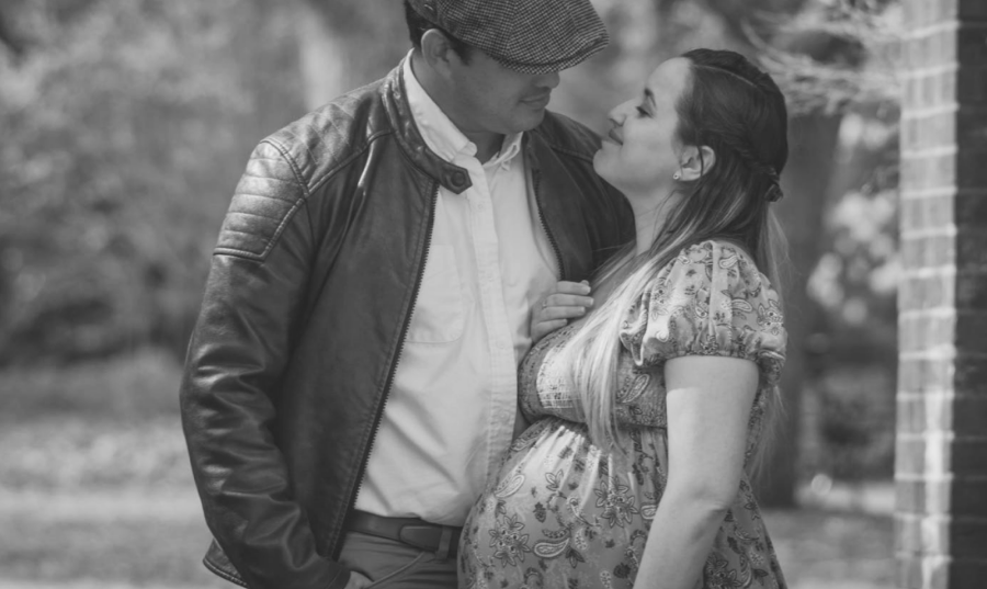 A black and white photograph of a man wearing a newsboy cap looking at a pregnant woman who is looking up at him and smiling.