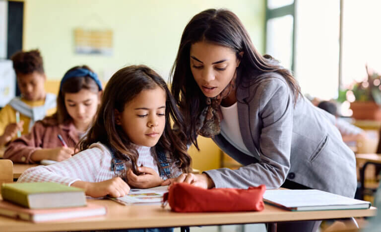 Teacher and student going over work in full classroom.