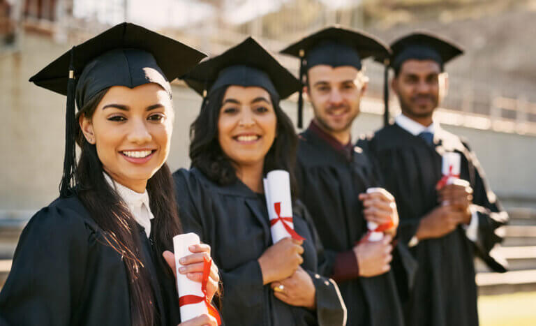 Four Latino students in their graduation caps and gowns holding diaplomas.