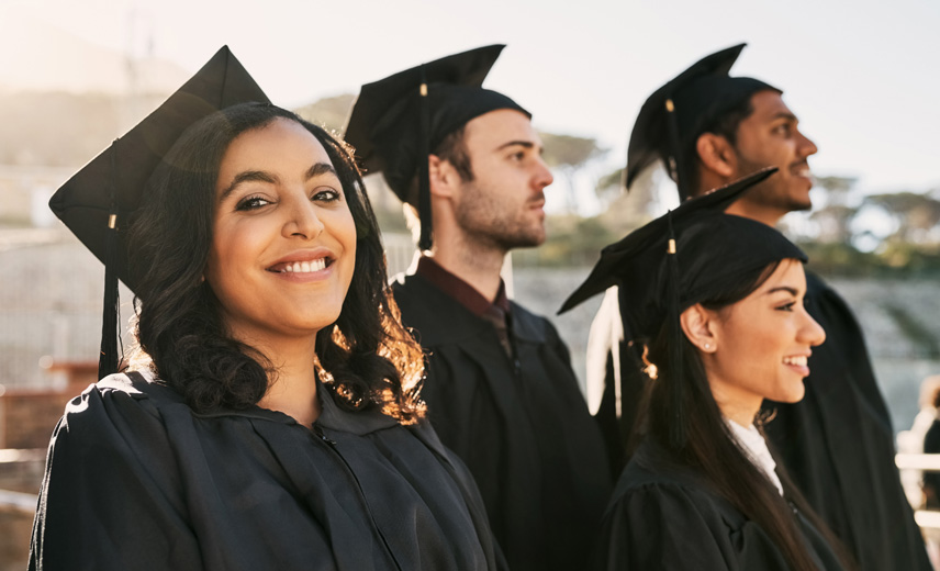 Four Latino students in their graduation caps with one student looking at the camera smiling.