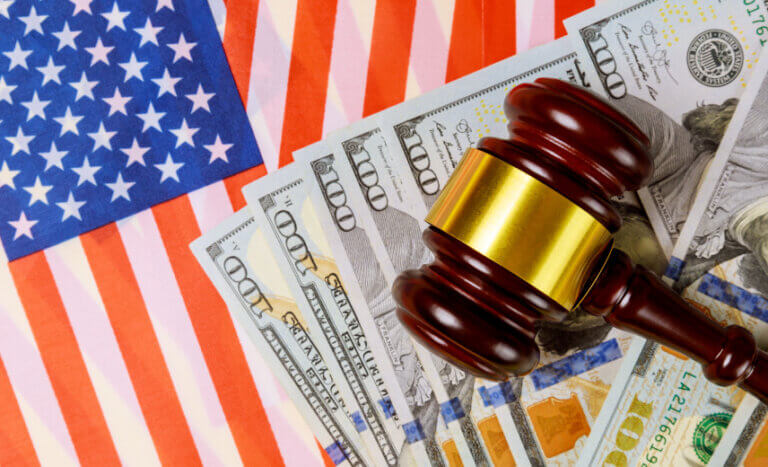 A U.S. flag, a gavel, and eight 100-dollar bills, symbolizing the economic costs of pursuing hardline state immigration policies.