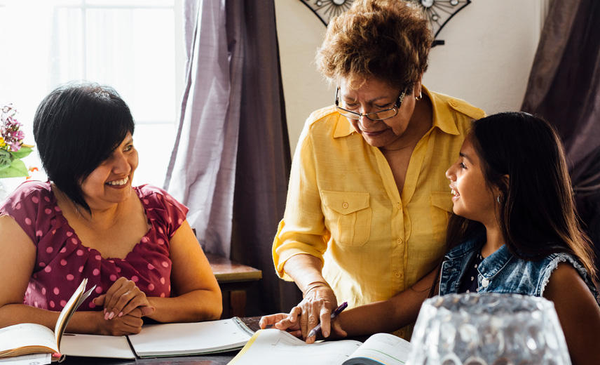 A Home Visitor along with a parent helping a young Latina girl with her homework.