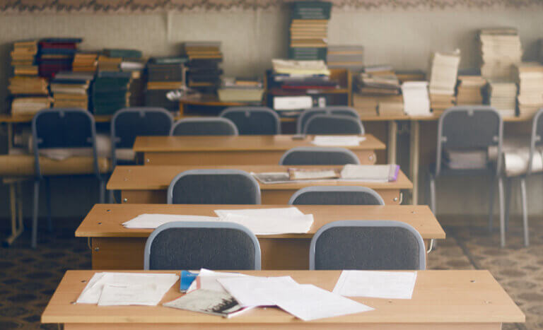 Empty classroom with papers and pencils left on desks.