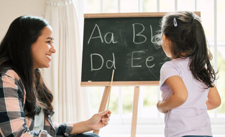 A Latina home visitor helps a preschool-aged girl learn her ABCs in English as part of a dual language learning approach.