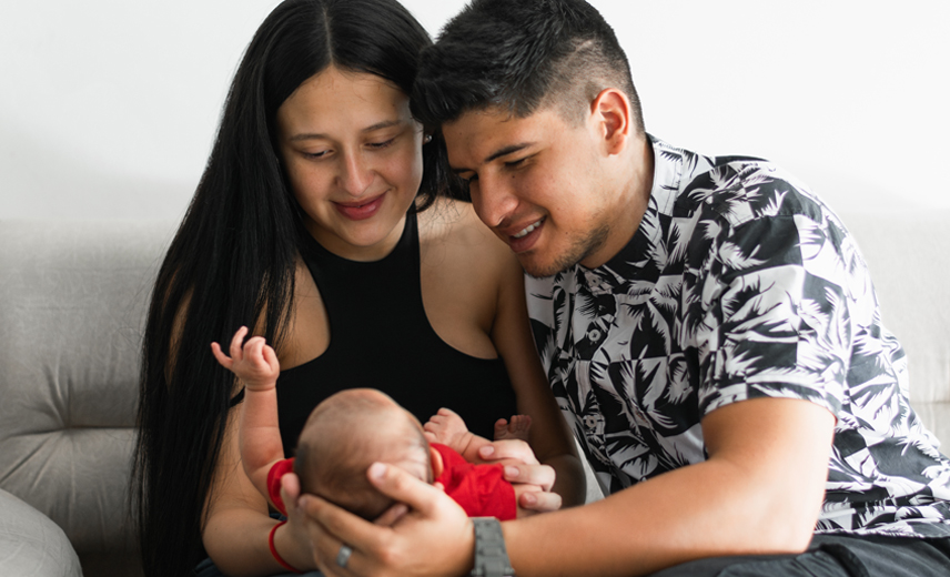 A loving Latino father and mother cradle their infant son, smiling warmly at their baby. This heartwarming family moment captures the joy of parenthood and the bond between parents and child.