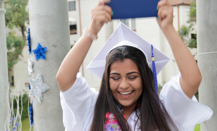 Excited Latina in graduation cap and gown celebrating with her college degree, representing the impact of financial aid.