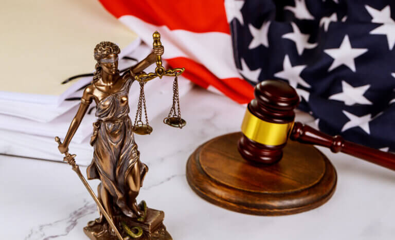 A statue of Lady Justice standing in front of a gavel and administrative document folders on a lawyer’s desk, symbolizing law, order, and judicial oversight.