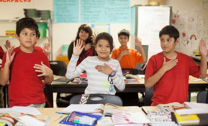 Three students in a classroom raising their hands, reflecting engagement in an English language learning environment.