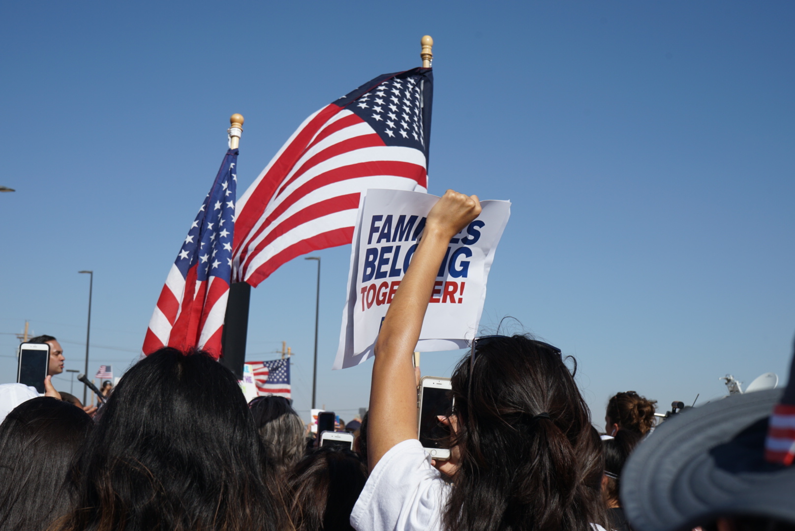 Texas Protest with american flags, and woman holding sign "Families Belong Together"